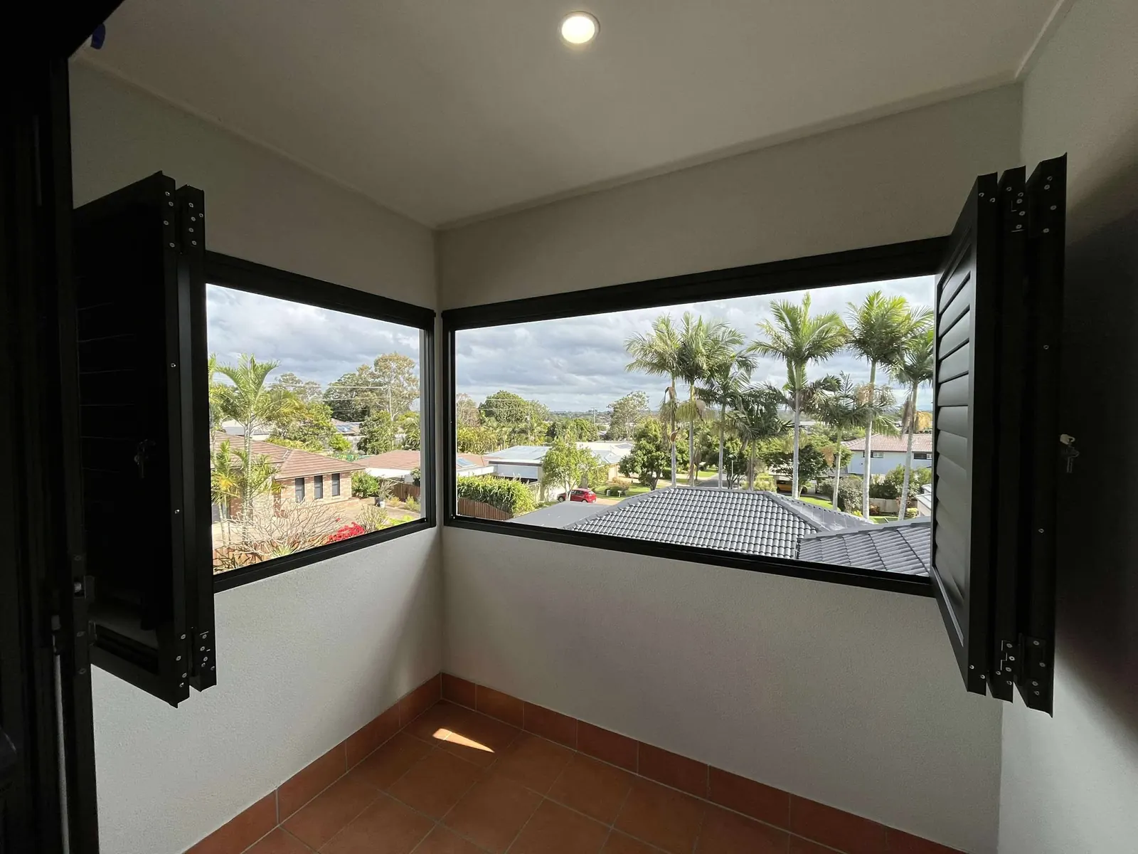 A corner bedroom with black Guardian shutters swung open to the view of the street and palms