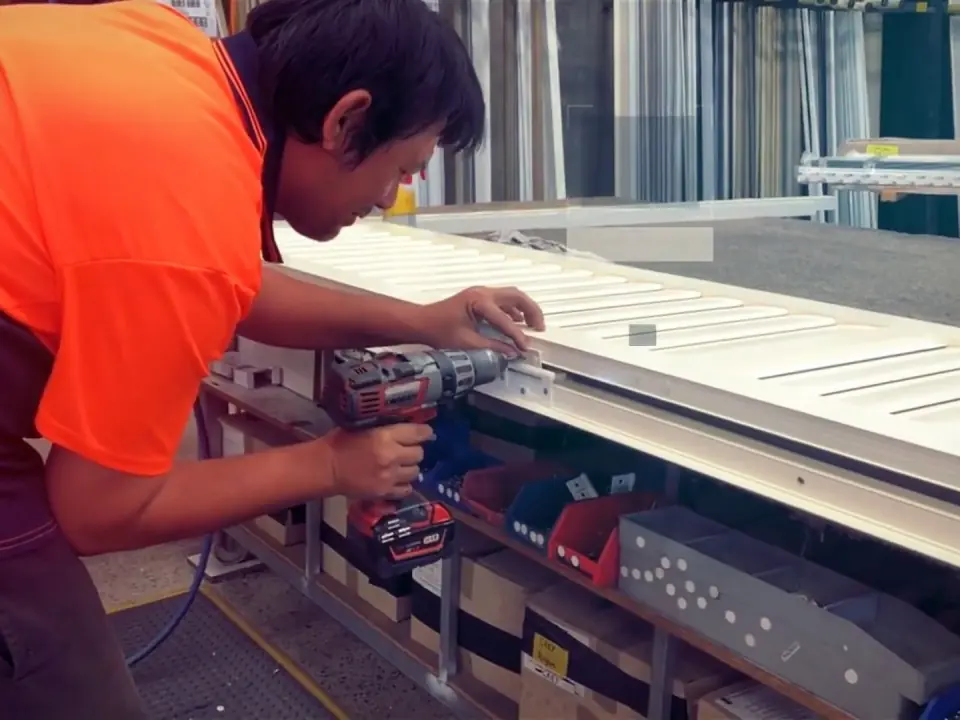 A Guardian worker in hi-vis assembling a white aluminium shutter panel at the workshop bench